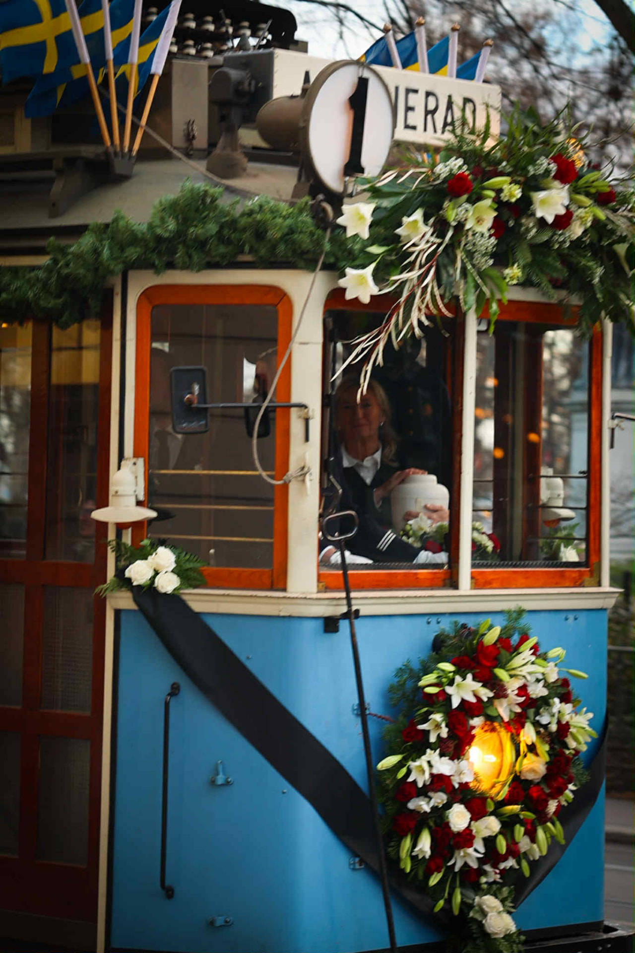 En spårvagn dekorad med grangrenar, vita och röda blommor och en krans – en unik sista färd genom stan