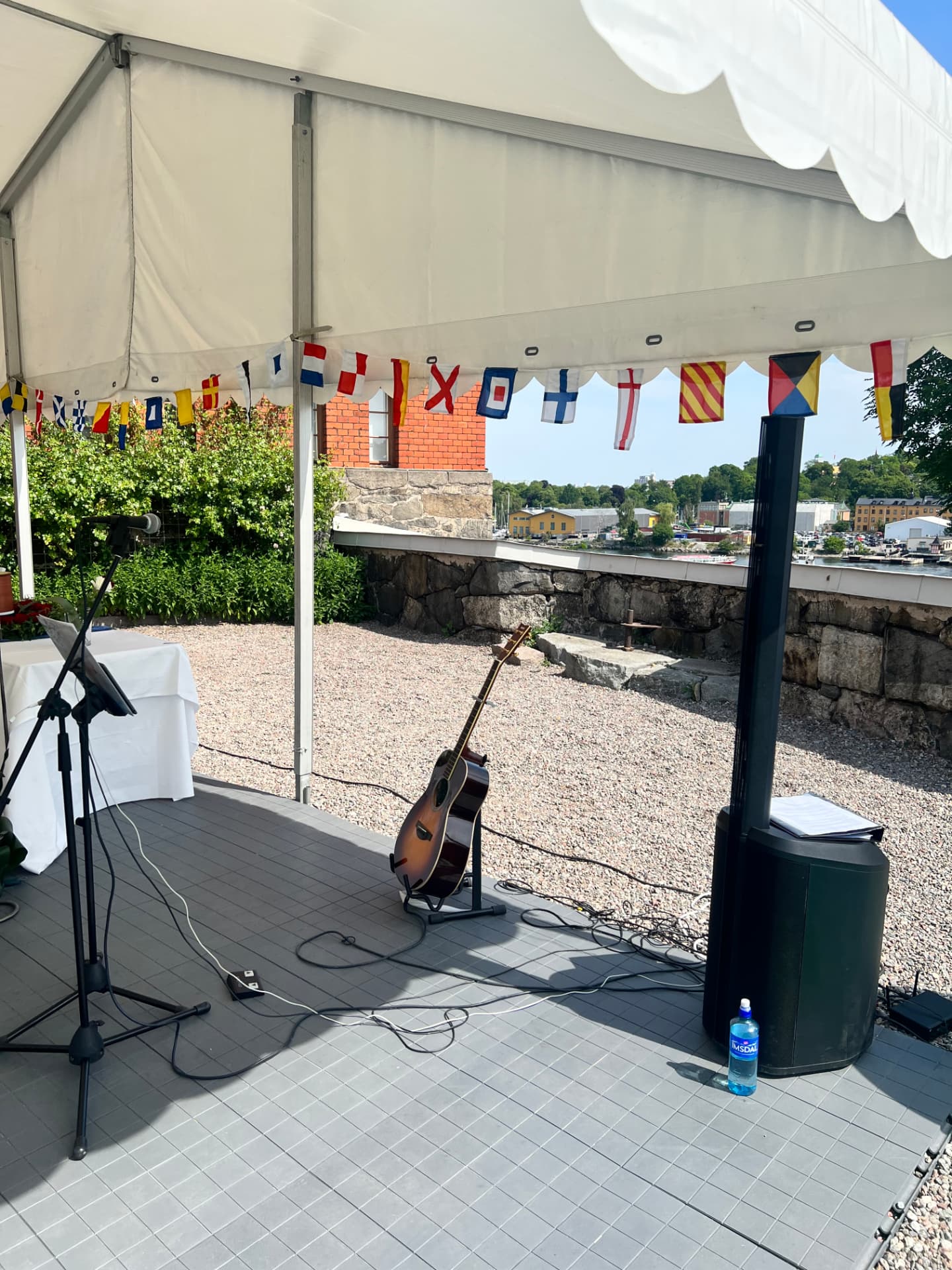 Gitarr och musikanläggning under vitt partytält vid havet, redo för en ceremoni