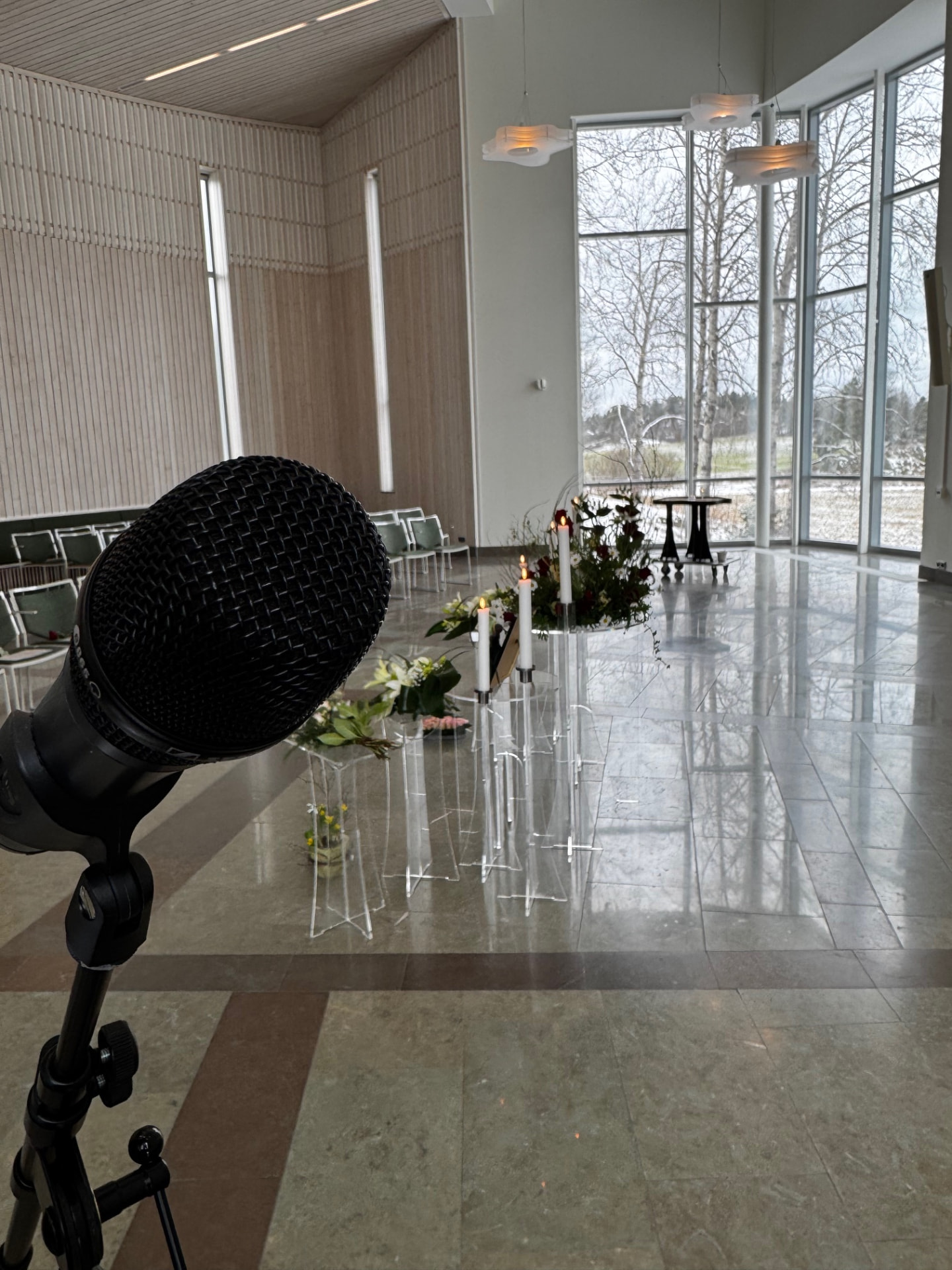 En borgerlig begravningsceremoni i Österhaninge med mikrofon, levande ljus och blommor i en ljus lokal med utsikt över naturen